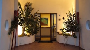 A hallway with a door leading to a room, flanked by plants and a wall-mounted number sign. - Hotel Il Gabbiano (La Maddalena)