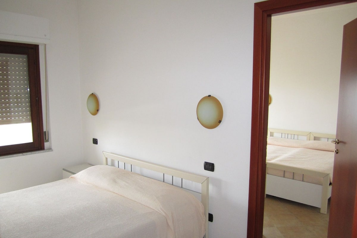 Een slaapkamer met een enkel bed, een raam met zonwering en een spiegel aan de muur.