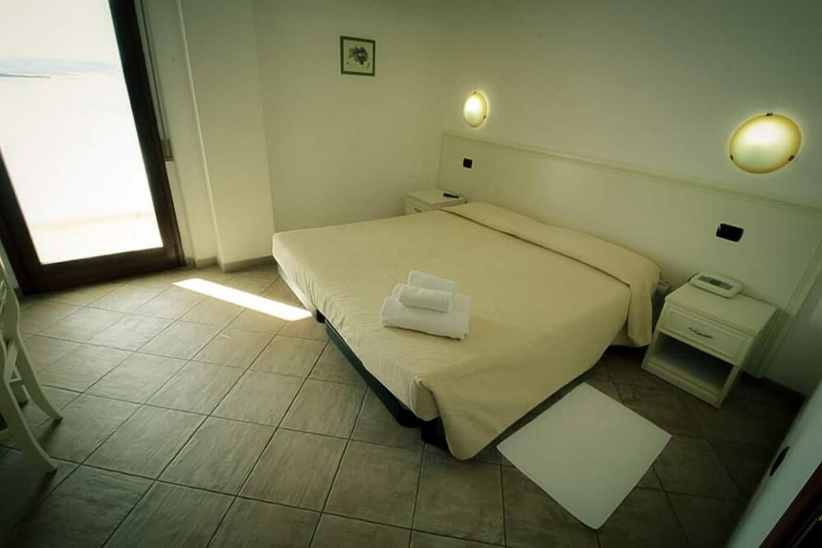 Een hotelkamer met een bed, nachtkastje, wandlamp en een deur naar een balkon.