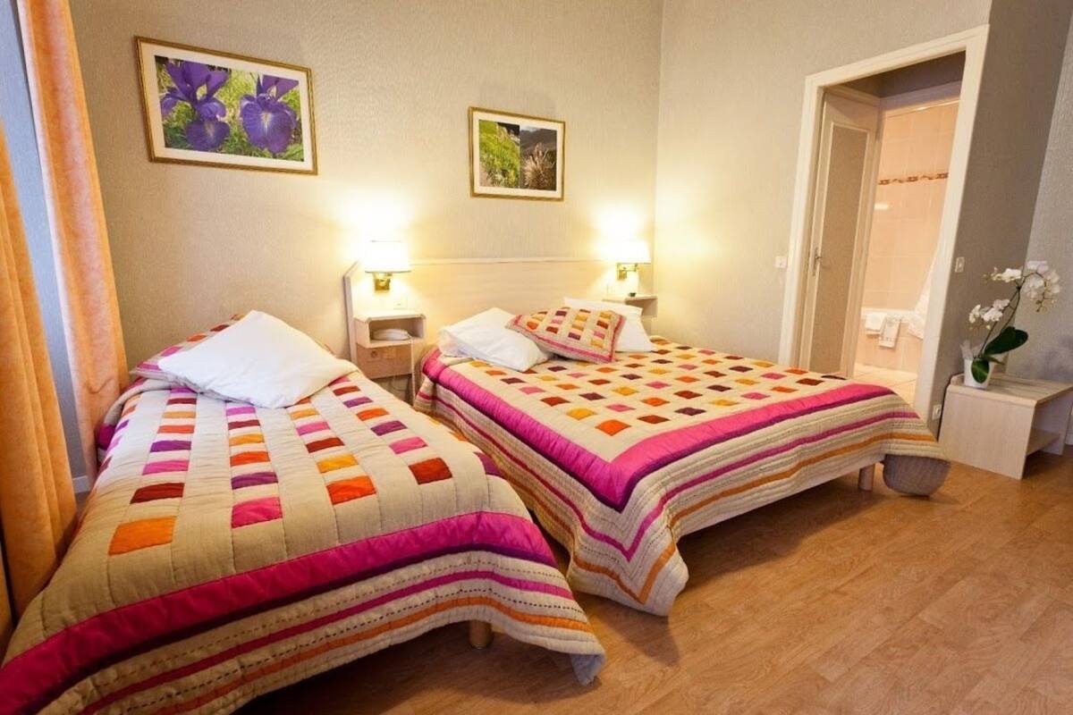 Quarto com duas camas, cada uma com colcha acolchoada, luminárias de cabeceira e quadros nas paredes.