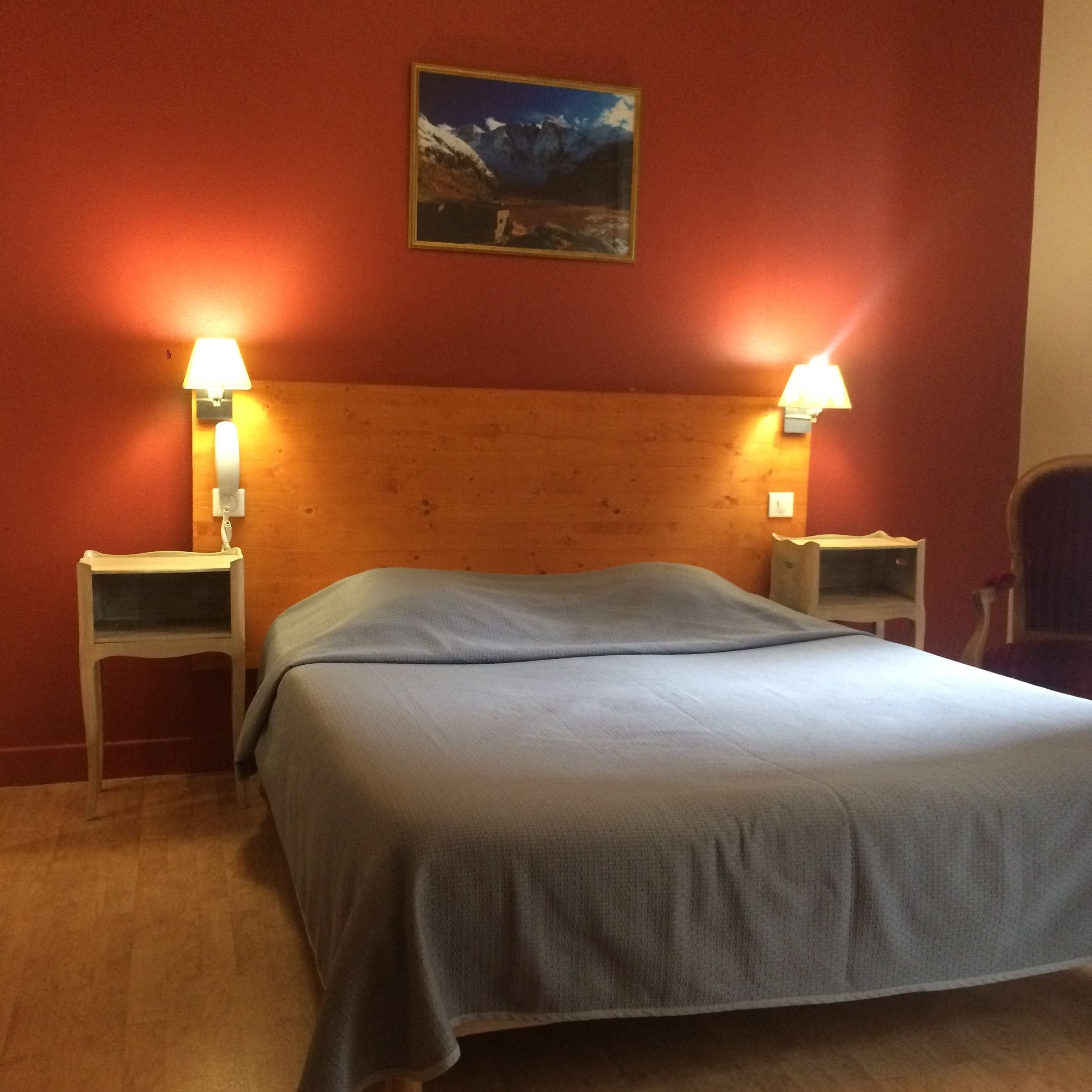 Una habitación con cama, dos lámparas de noche, cabecera de madera y un cuadro en la pared.