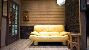 Una habitación con sofá de cuero amarillo, suelo de madera, pared decorada con piedra, mesita de madera y una puerta con panel de vidrio.