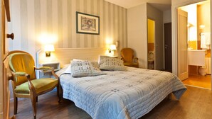 Habitación de hotel con una cama grande, dos mesitas de noche con lámparas, una silla y una puerta que da a un baño.