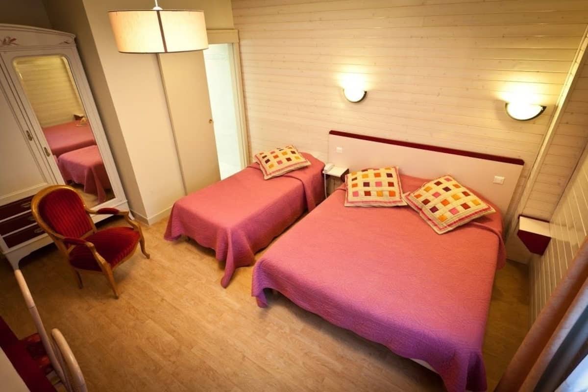 Quarto de hotel com duas camas, uma cadeira, um espelho e um abajur.