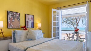 Un dormitorio con cama, lámparas de noche, vista a la playa y una puerta que da al exterior.
