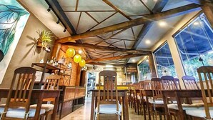 Amplia habitación con vigas de madera en el techo, una zona de bar con sillas y ventanas amplias que dejan entrar luz natural.