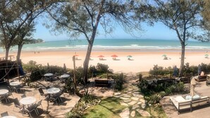 Un patio frente a la playa con mobiliario exterior y sombrillas, con vista a una playa de arena y al océano.