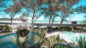 Zona junto a la piscina con mesa de vidrio, sillas y vista a la playa.