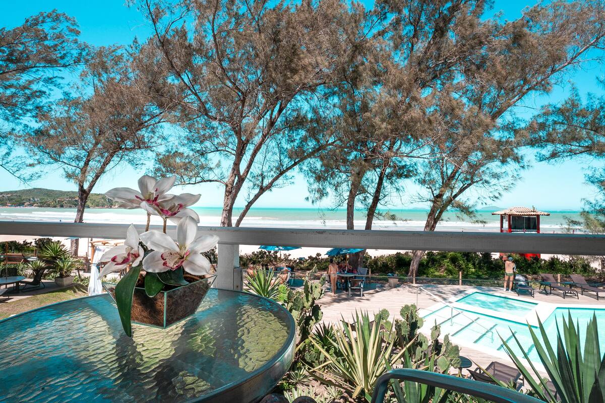 Zona junto a la piscina con mesa de vidrio, sillas y vista a la playa.
