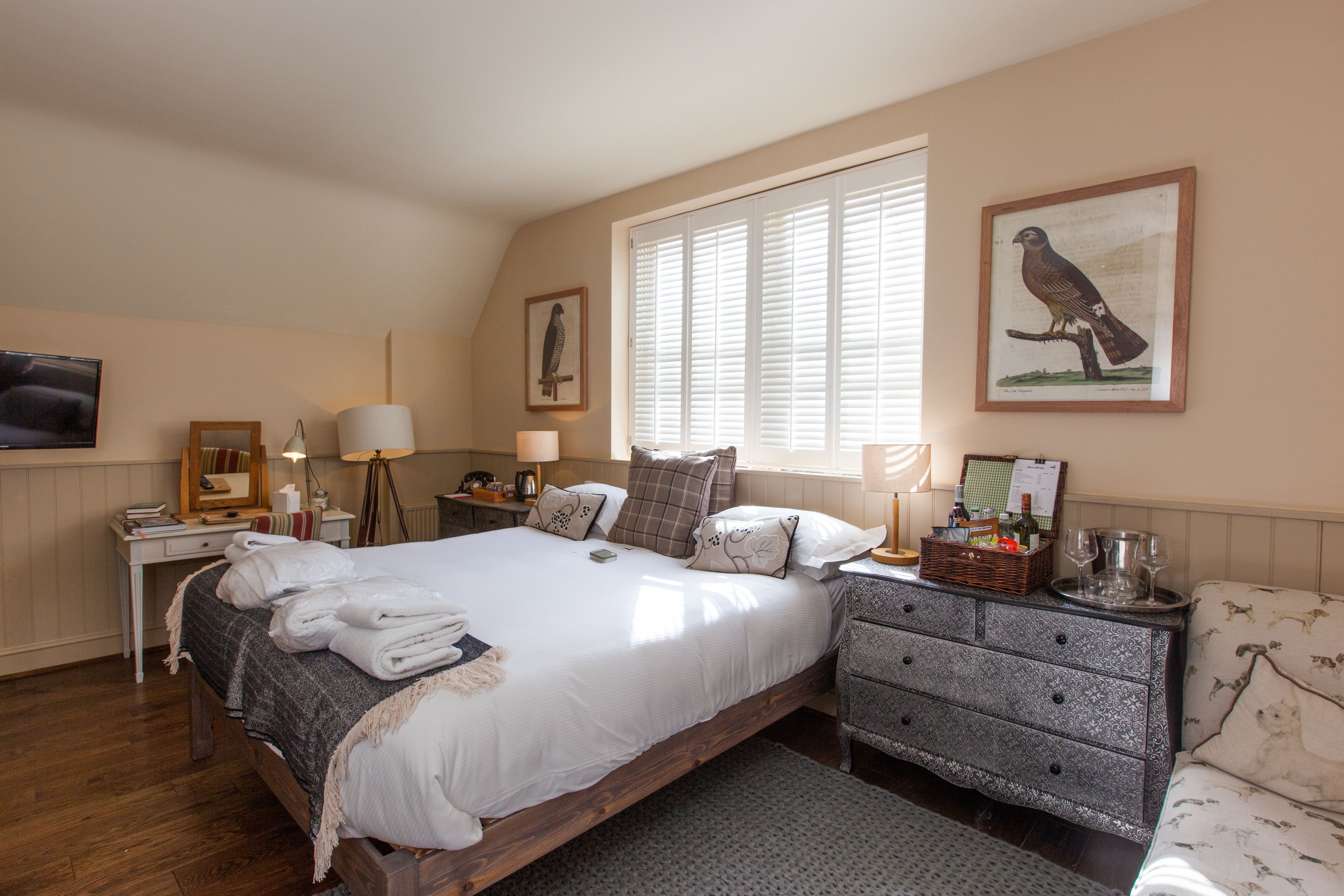 A bedroom with a large bed, bedside tables, a dresser, and a window with blinds.