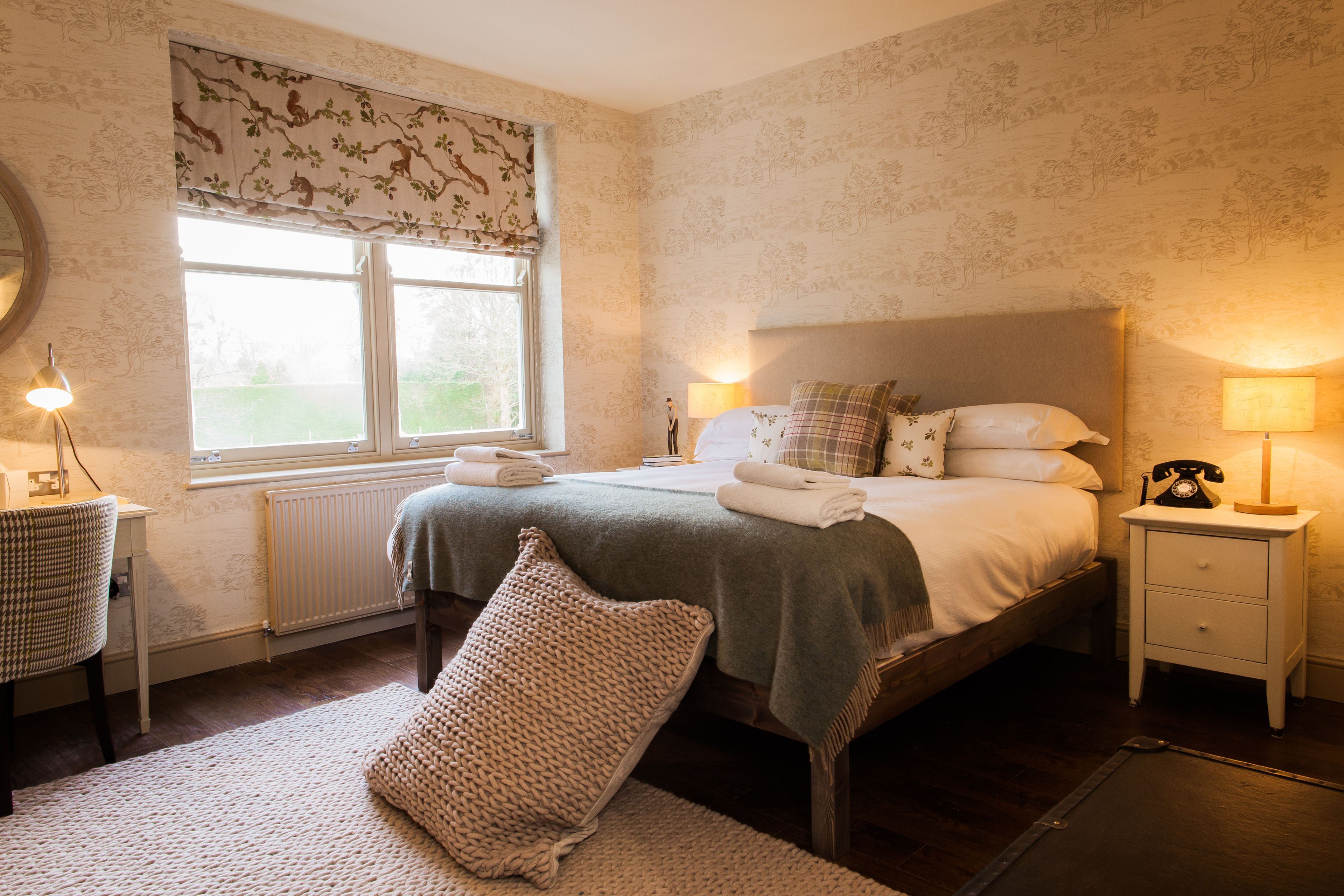 A bedroom with a bed, bedside tables, a lamp, a radiator, a window with curtains, and a patterned wall.