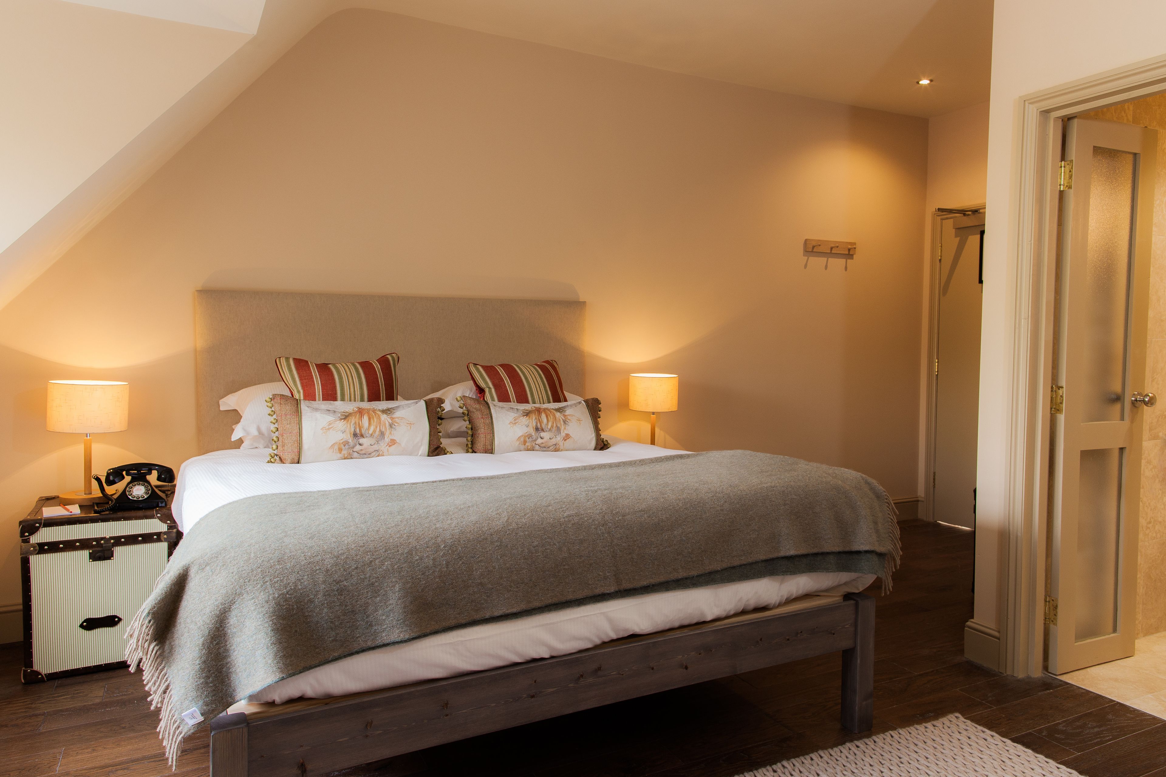 Ein Schlafzimmer mit einem großen Bett, Nachttischlampen, einem Koffer und einer Tür zum Badezimmer.