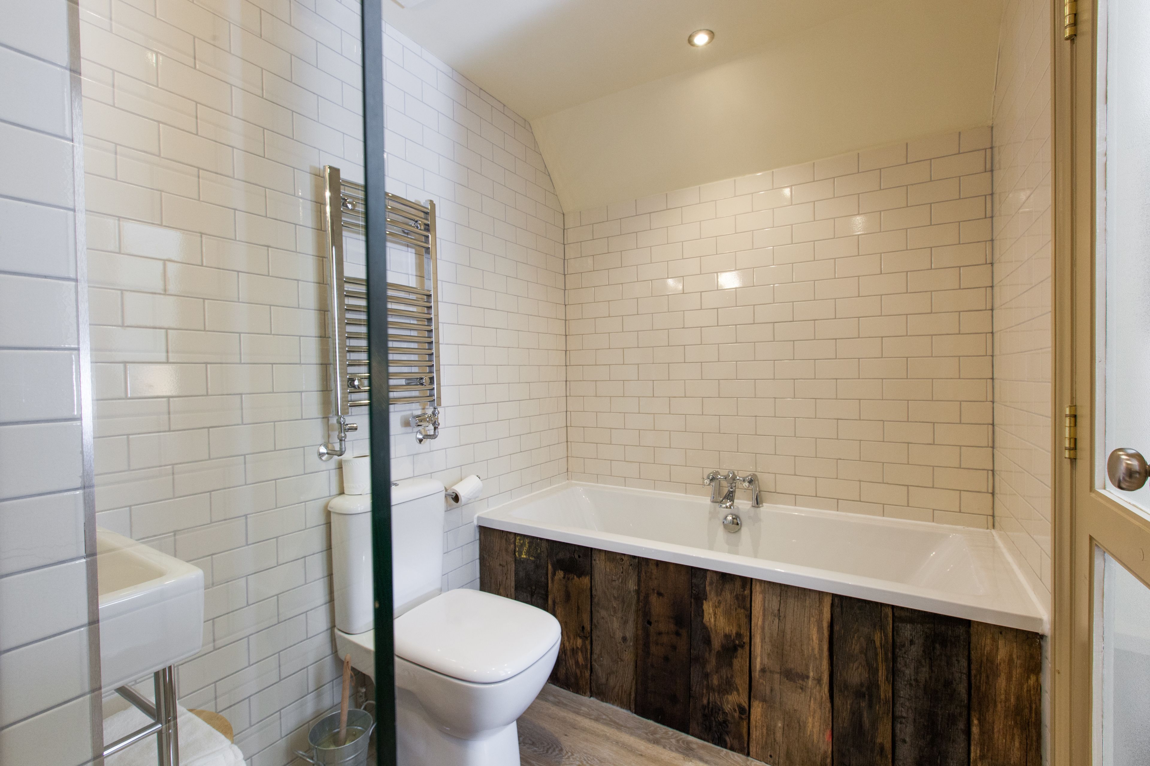 A bathroom with white tiled walls, a wooden floor, a white toilet, and a white bathtub.