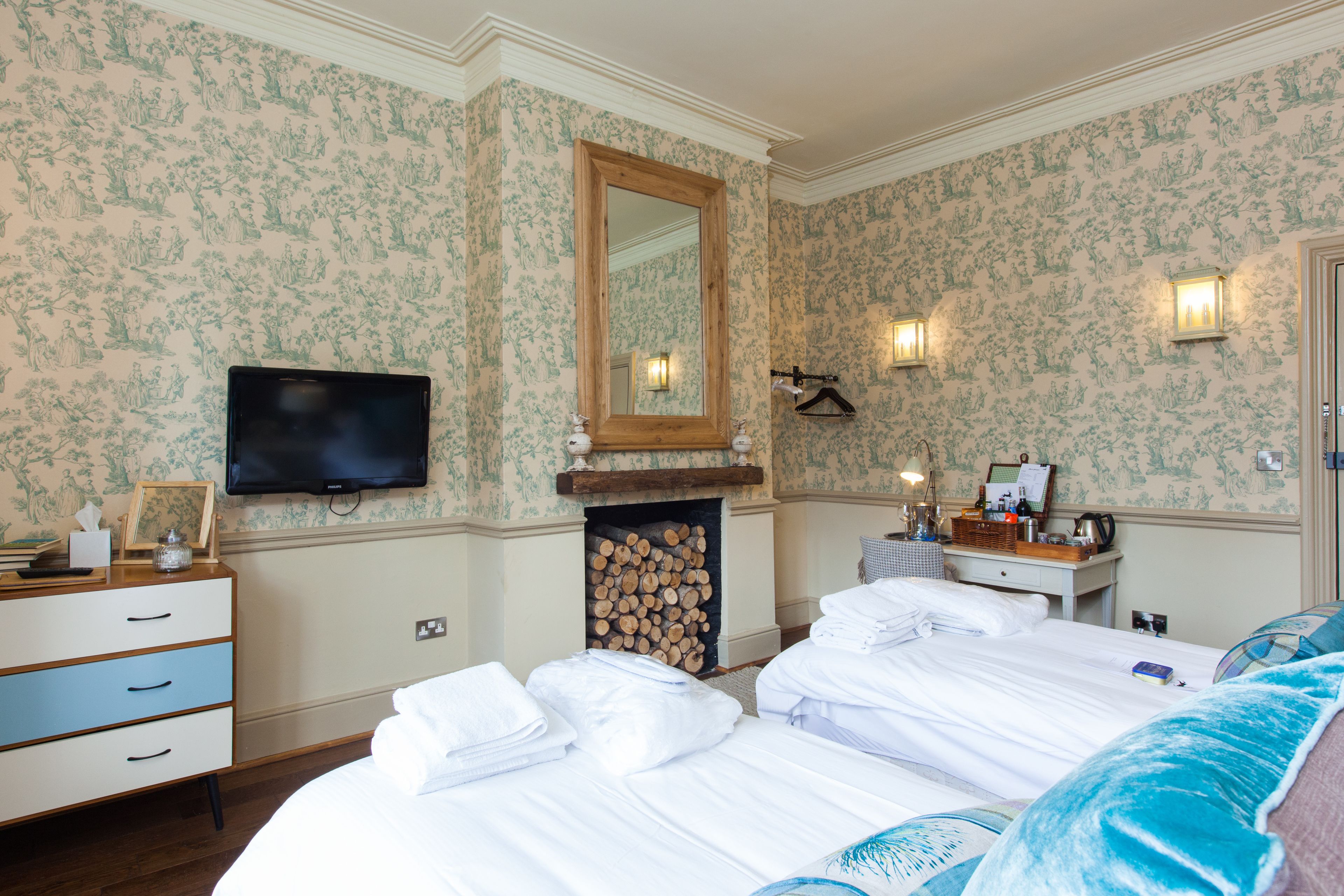 A hotel room with a large bed, a television, a fireplace, and a mirror.