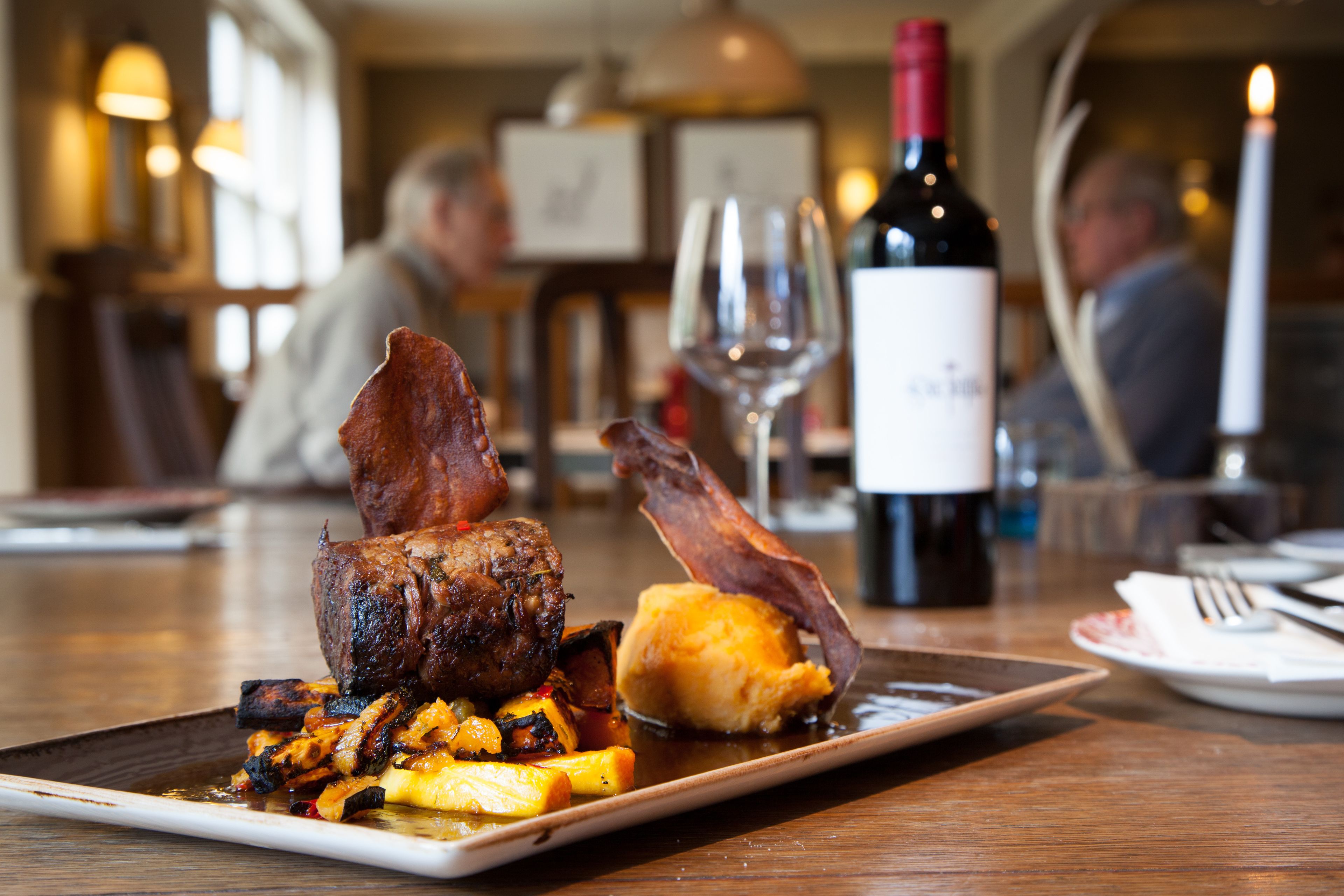 A dining table with a plate of food, a bottle of wine, and a candle.