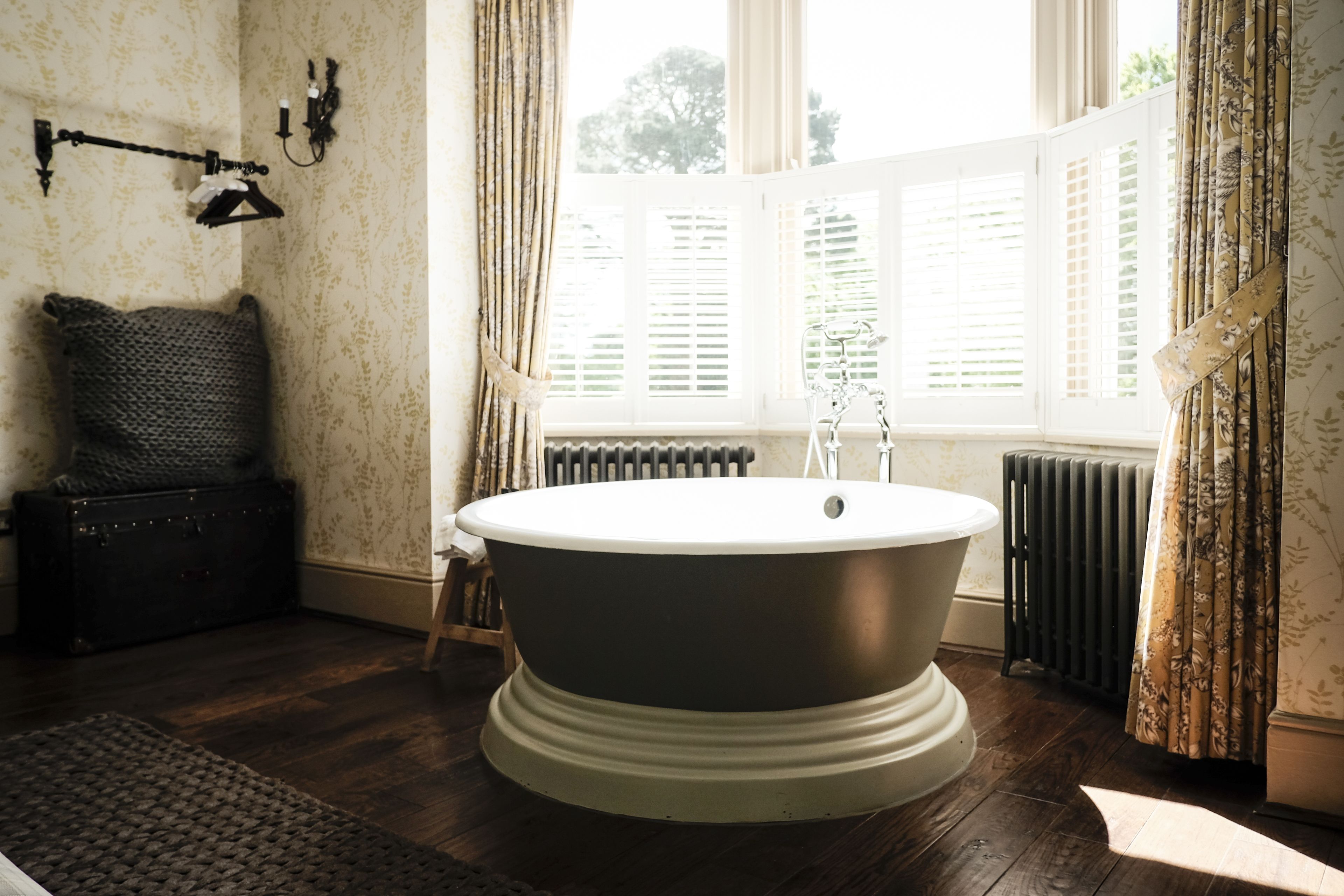 A classic bathroom with a freestanding bathtub, a radiator, and a window with shutters.