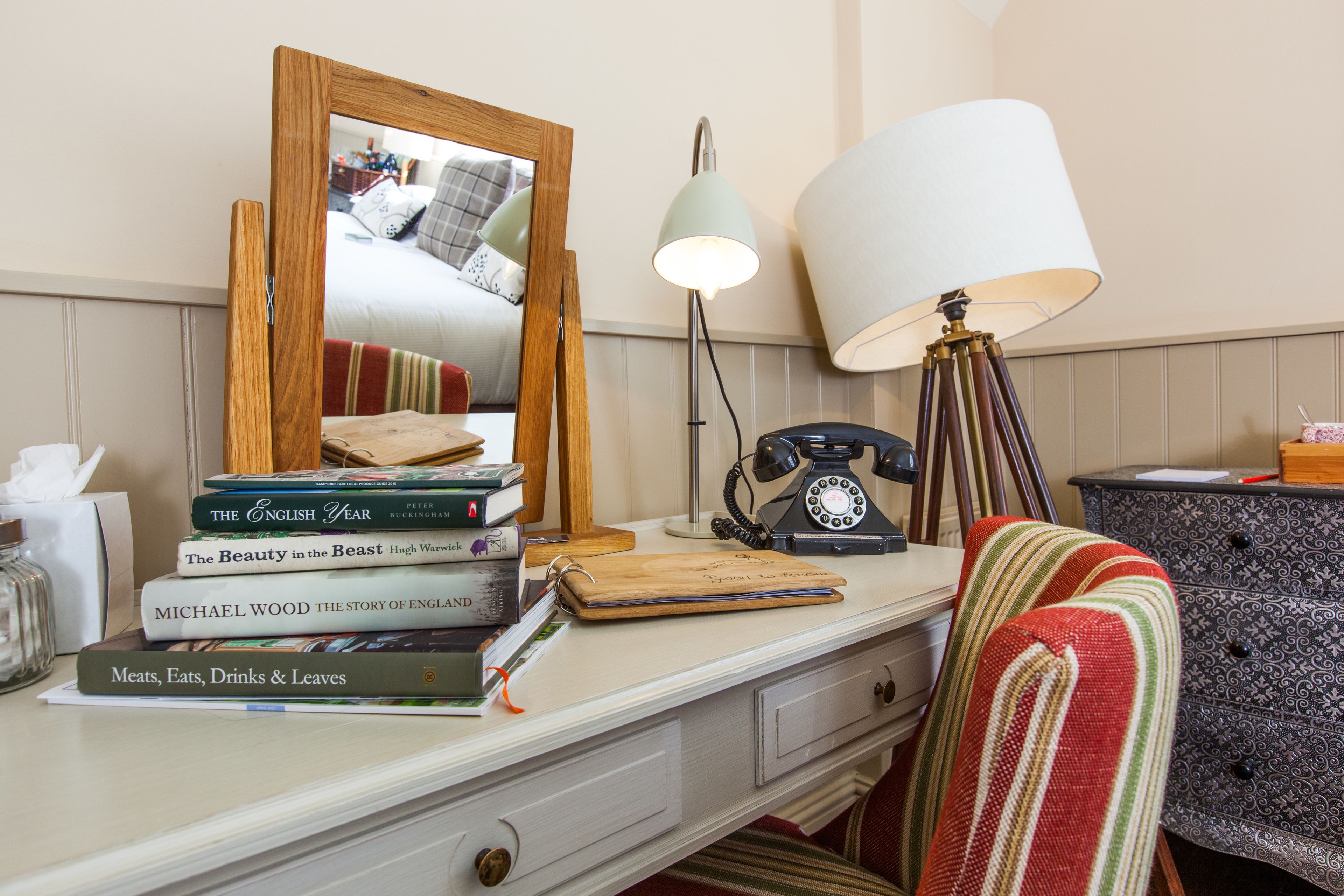 A neatly organized desk with a mirror, books, a lamp, and a telephone.