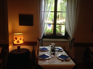 A dining table set for four with a lamp on the left, a window with curtains, and a radiator below. - Locanda dei Baroni (Poppi)