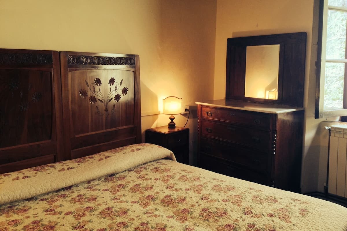 A bedroom with a bed, a dresser, a nightstand, a mirror, and a wall-mounted cross.
