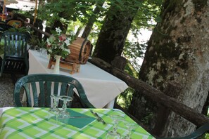 An outdoor dining area with a table set for two, surrounded by greenery and trees. - Locanda dei Baroni (Poppi)