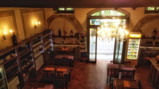 A cozy restaurant interior with wooden tables and chairs, a wine rack, and a chandelier. - Locanda dei Baroni (Poppi)