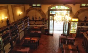 A cozy restaurant interior with wooden tables and chairs, a wine rack, and a chandelier.