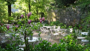 An outdoor garden area with metal tables and chairs, surrounded by greenery and a stone wall. - Locanda dei Baroni (Poppi)