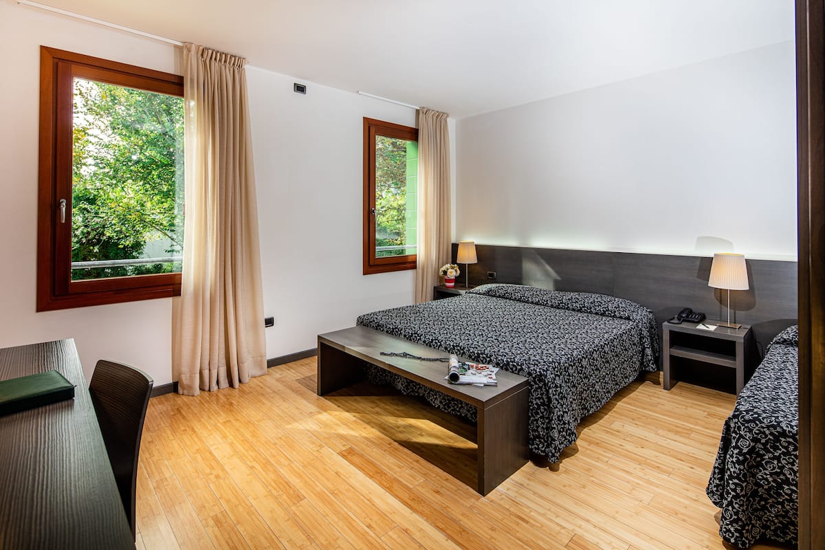 Ein Hotelzimmer mit Bett, Nachttischen, Schreibtisch und einem Fenster mit Vorhängen.