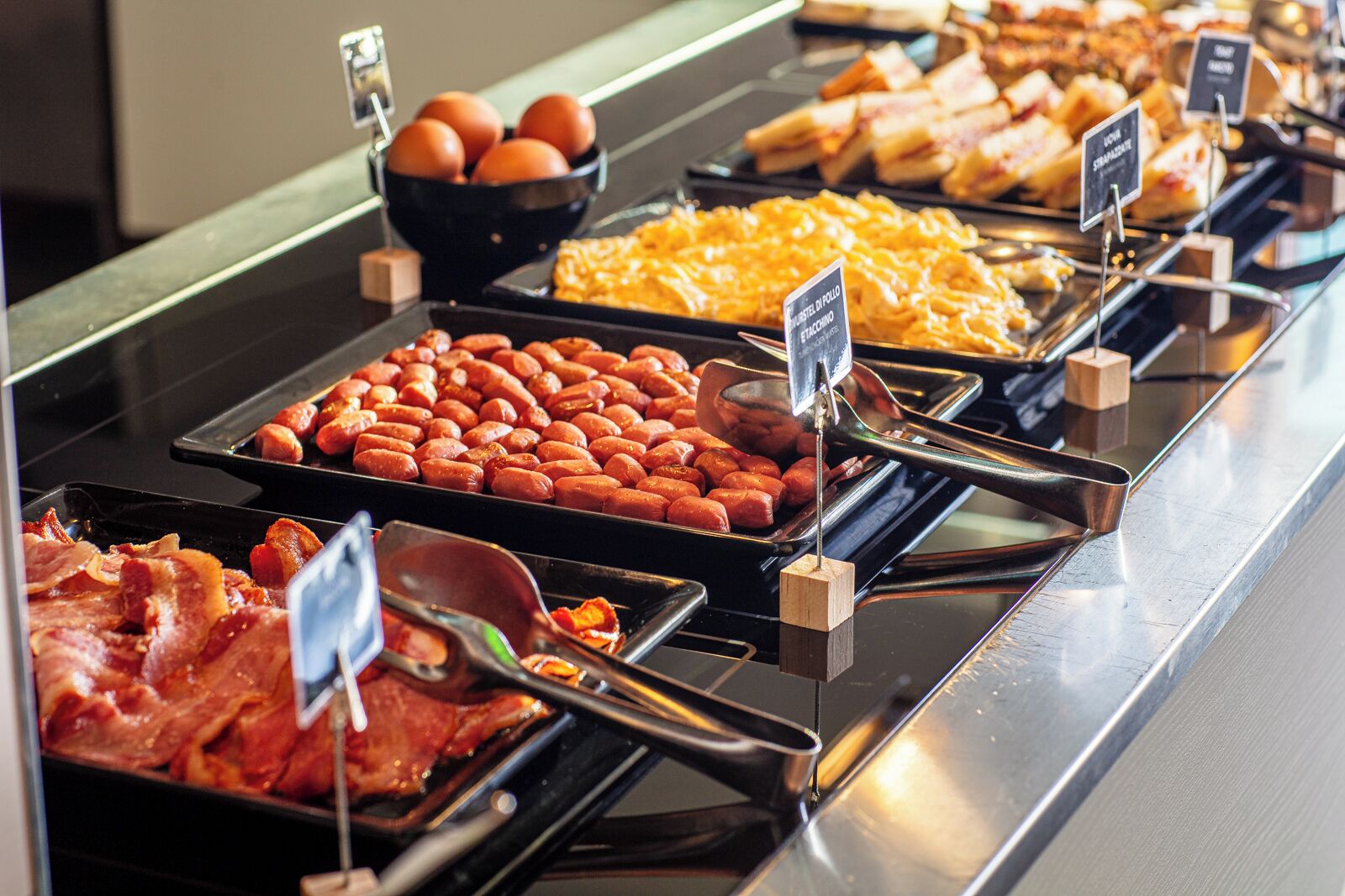 A buffet with various food items including sausages, eggs, and bacon.