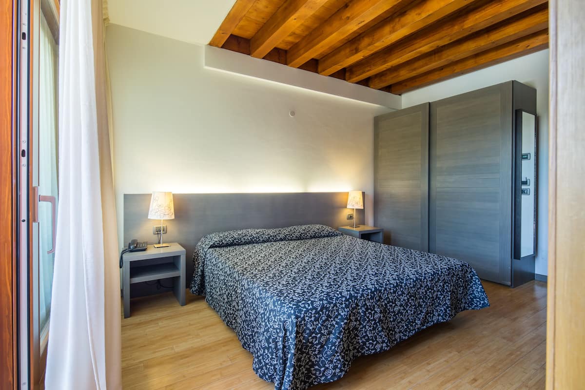 Ein Schlafzimmer mit einem Bett, Nachttischen, einem Kleiderschrank und einer Holzbalkendecke.