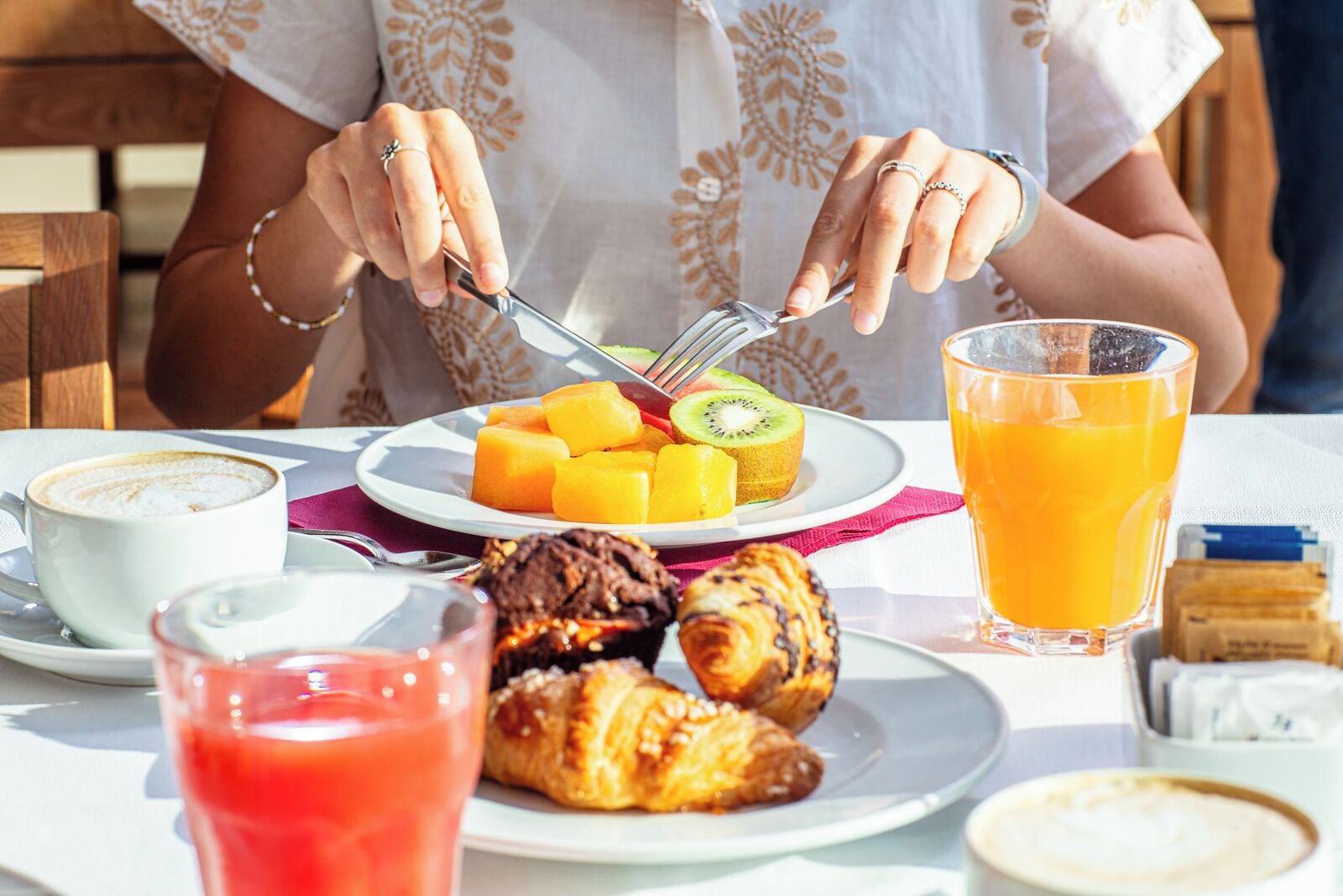 A breakfast setting with a plate of fruit, croissants, and a glass of orange juice.