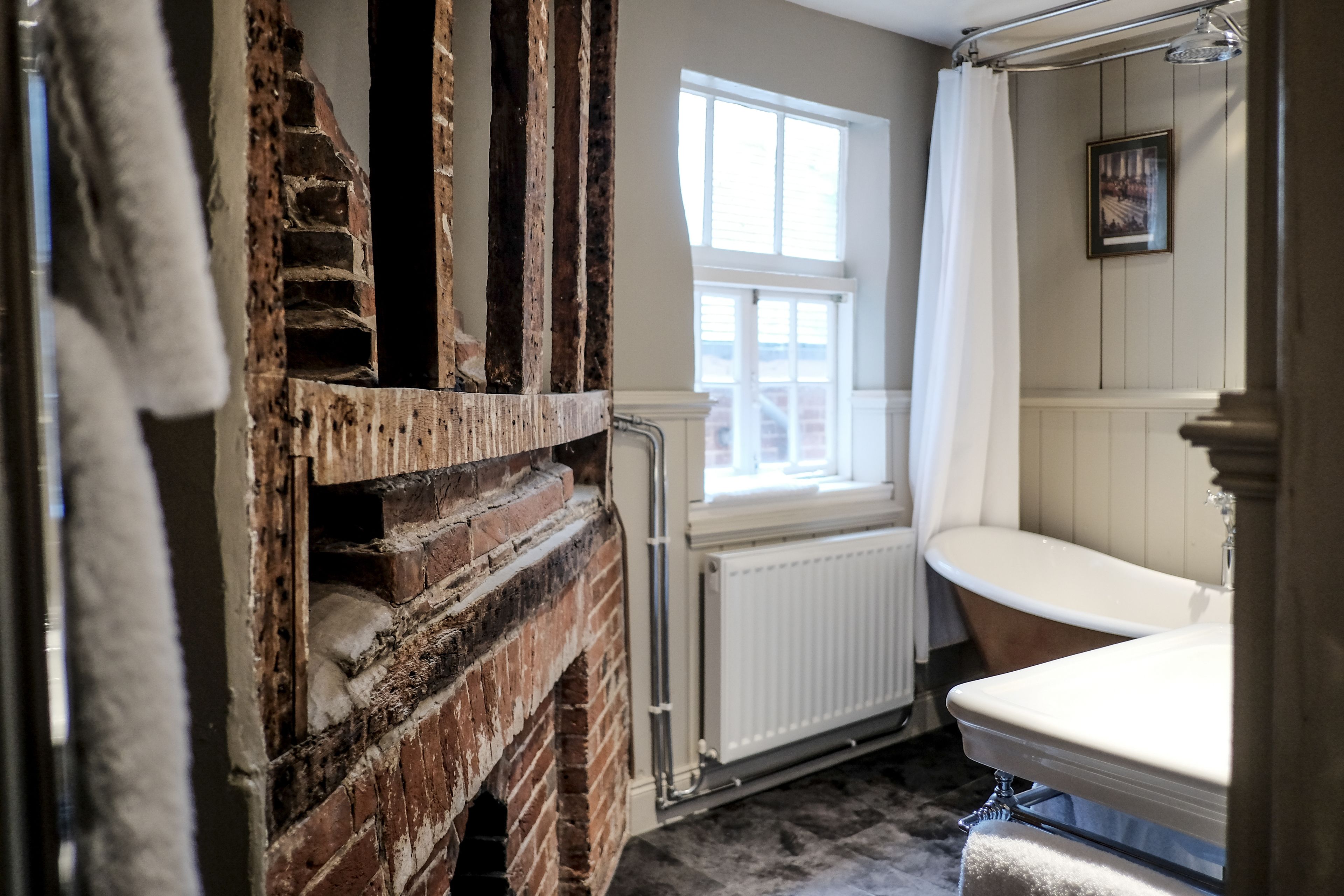 A bathroom with a vintage bathtub, a window, and exposed brick walls.