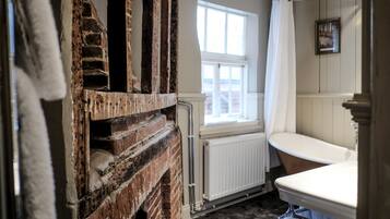 A bathroom with a vintage bathtub, a window, and exposed brick walls.