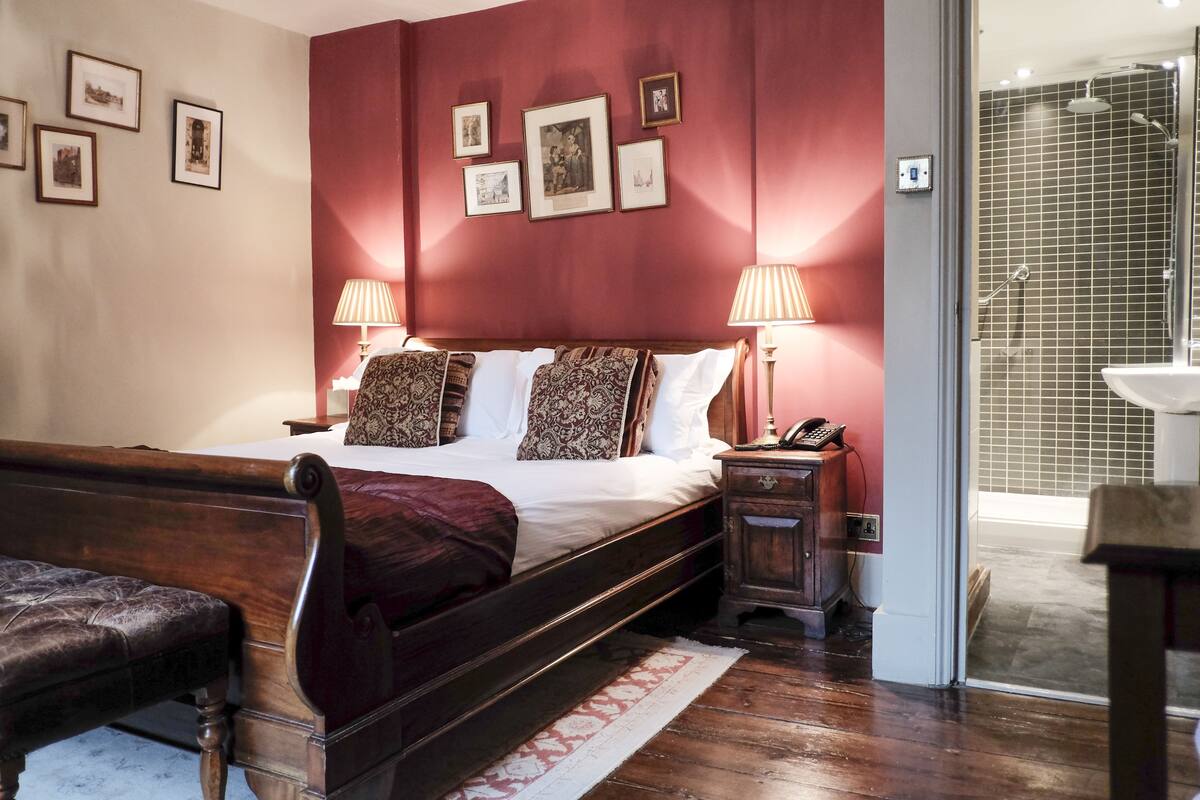 Quarto com cama de madeira, duas luminárias de cabeceira, mesa de cabeceira e um banco.