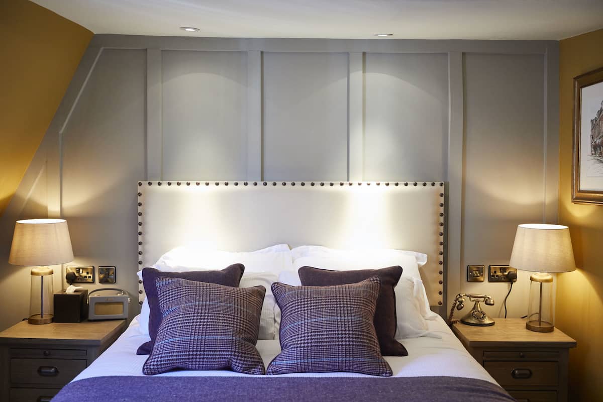 Quarto de hotel com uma cama grande, duas mesas de cabeceira, luminárias, um rádio e um quadro na parede.