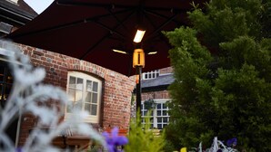 Een bakstenen gebouw met een grote parasol, een bankje en een bloemenrijke tuin.
