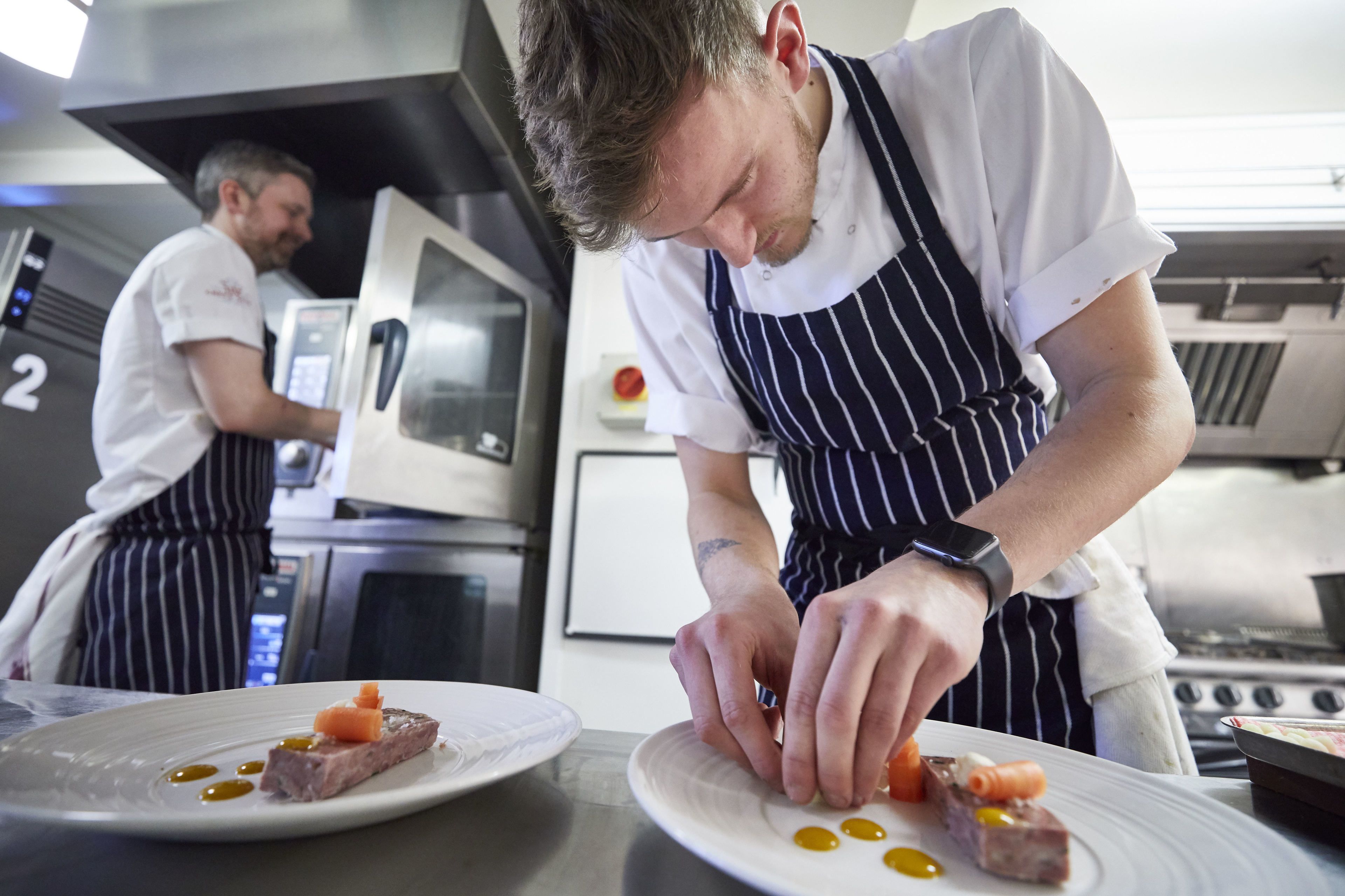 A chef preparing food in a professional kitchen with stainless steel appliances and a clean, organized layout.