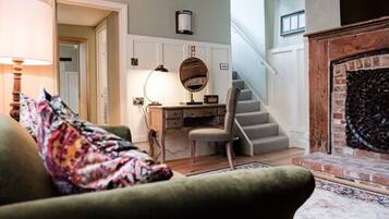 A cozy living room with a green armchair, a desk with a lamp, and a fireplace.