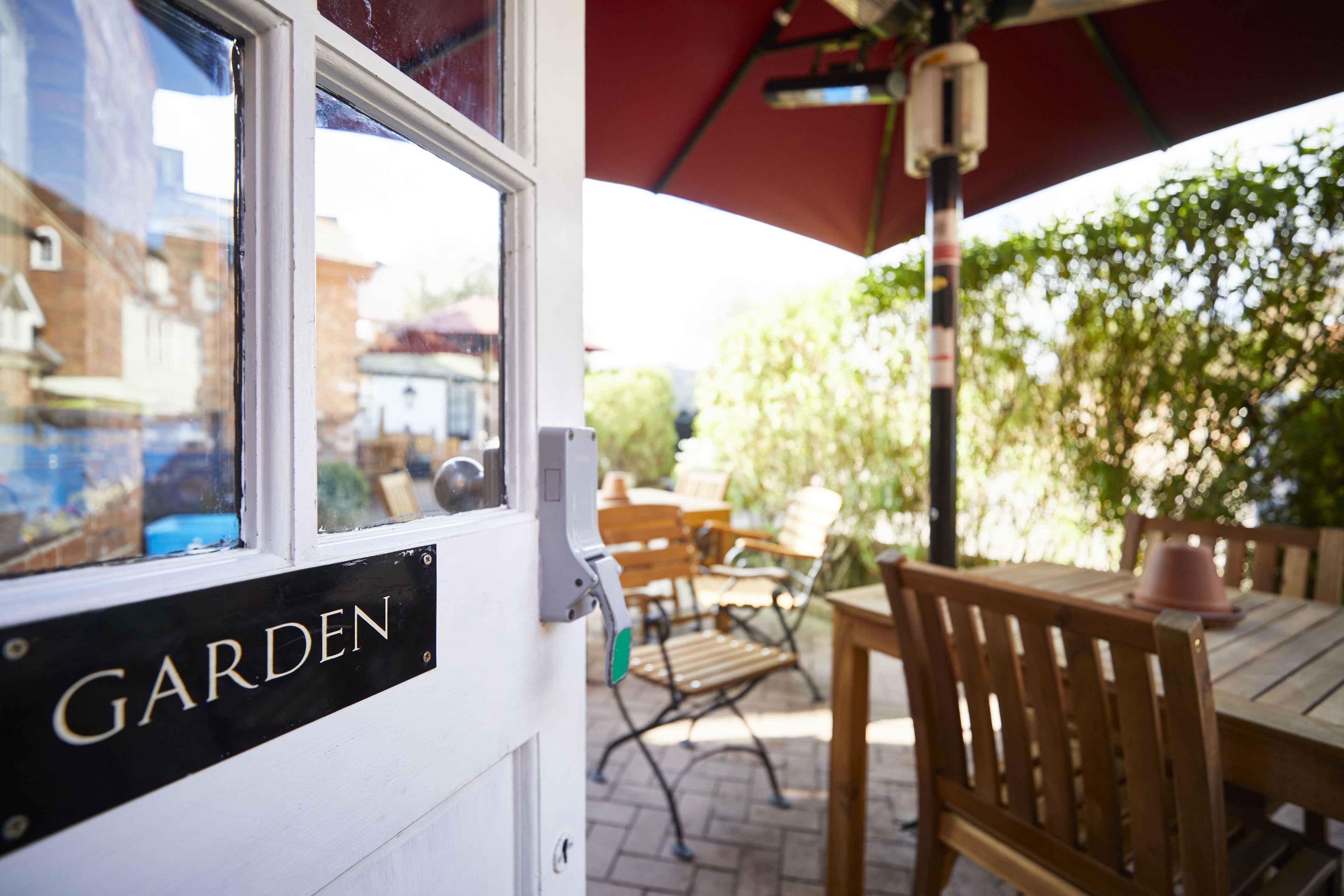 A door labeled "GARDEN" with outdoor seating and a red umbrella.