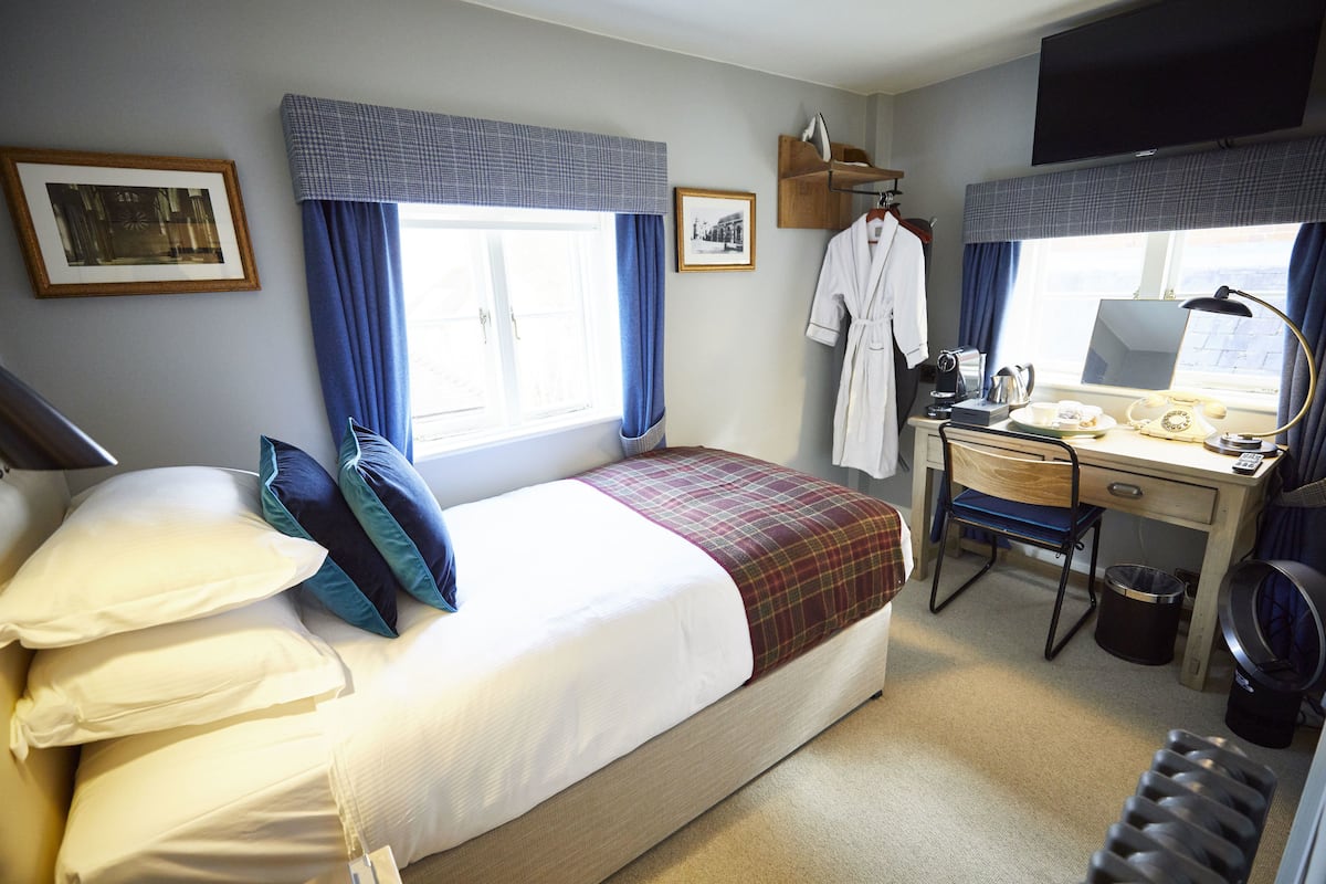 Quarto de hotel com cama, escrivaninha, cadeira, televisão e janela com cortinas.