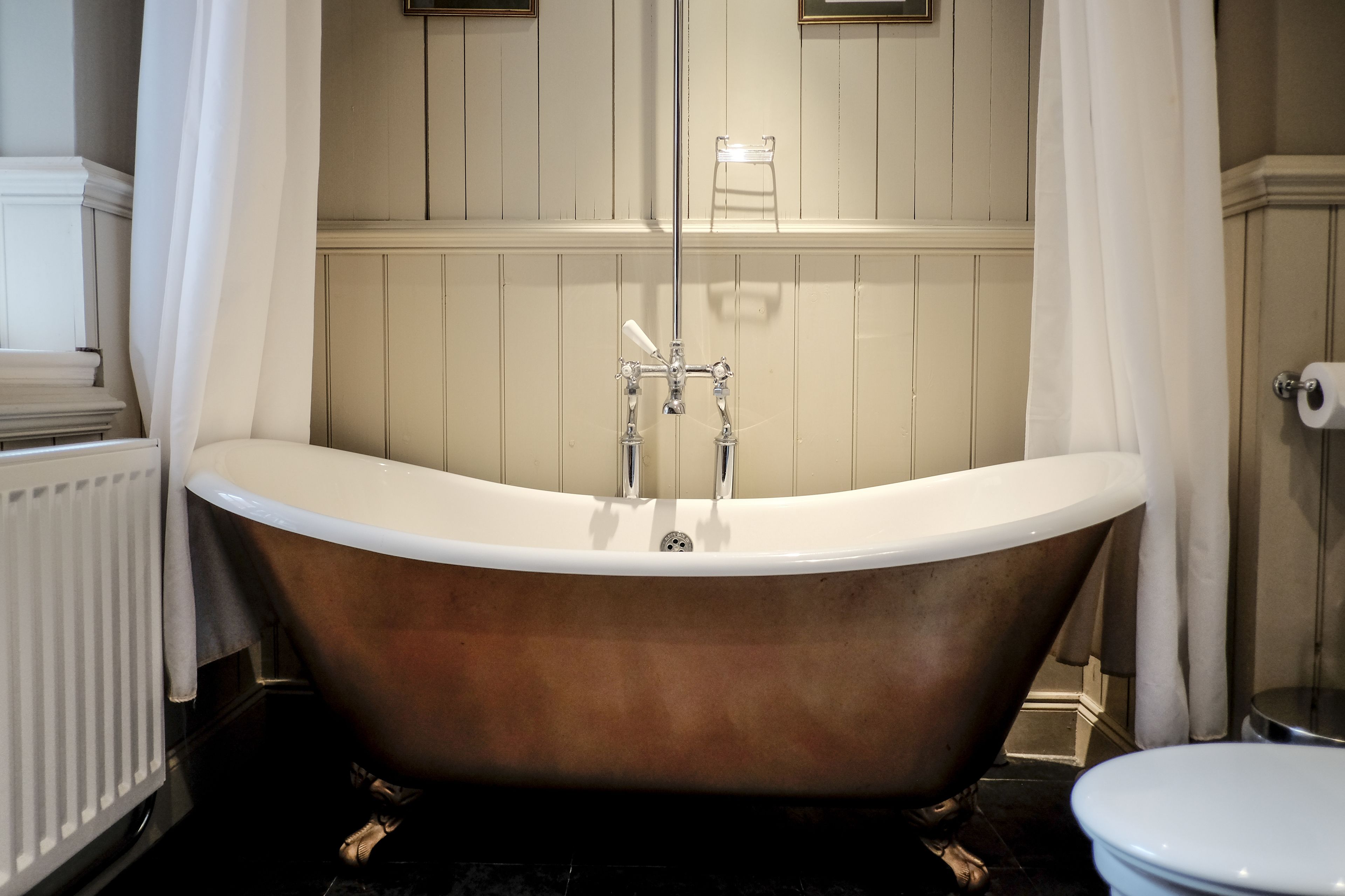 A bathroom with a freestanding bathtub, a toilet, and a radiator.