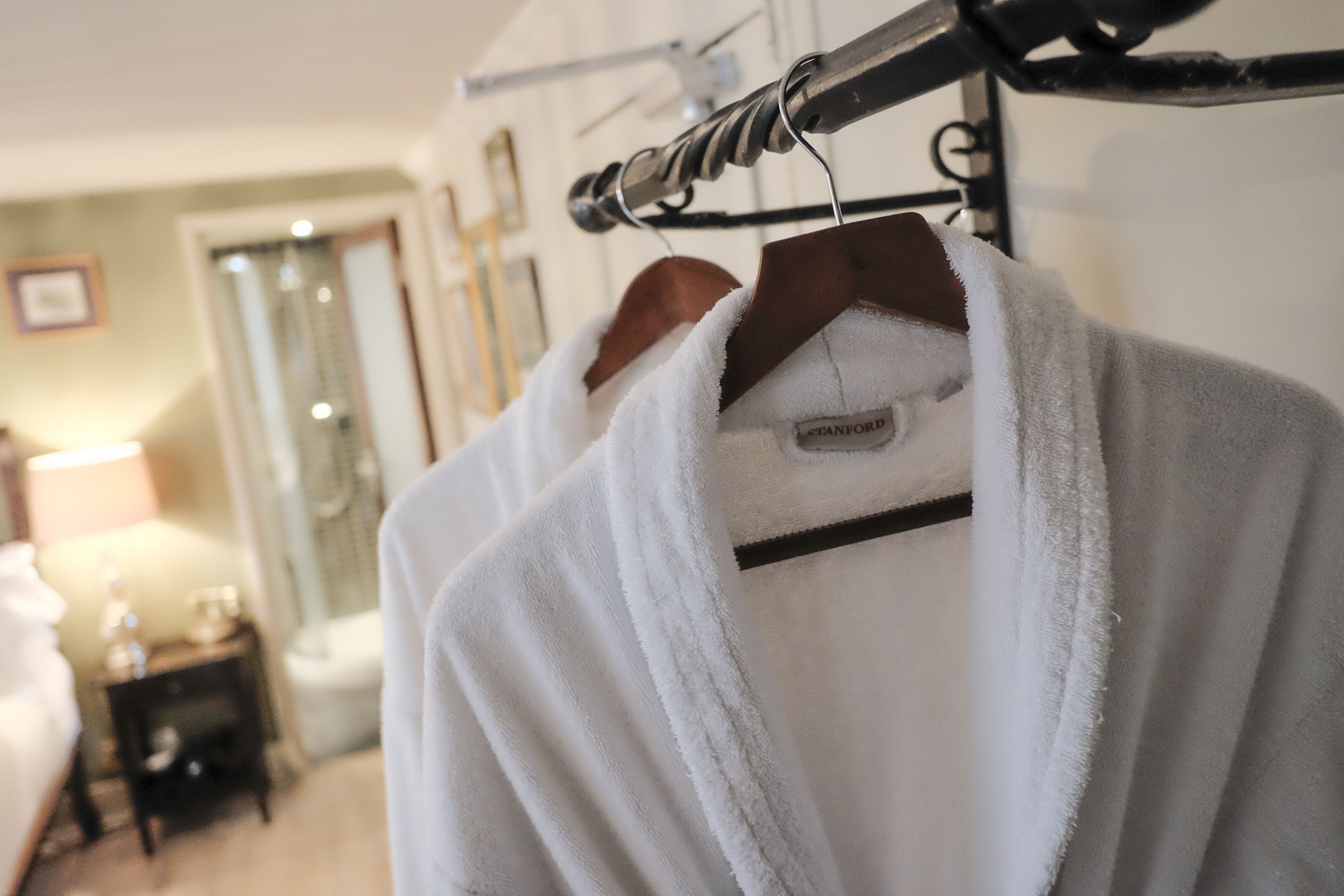 A hotel room with a robe hanging on a rack, a bed, a nightstand, and a lamp.