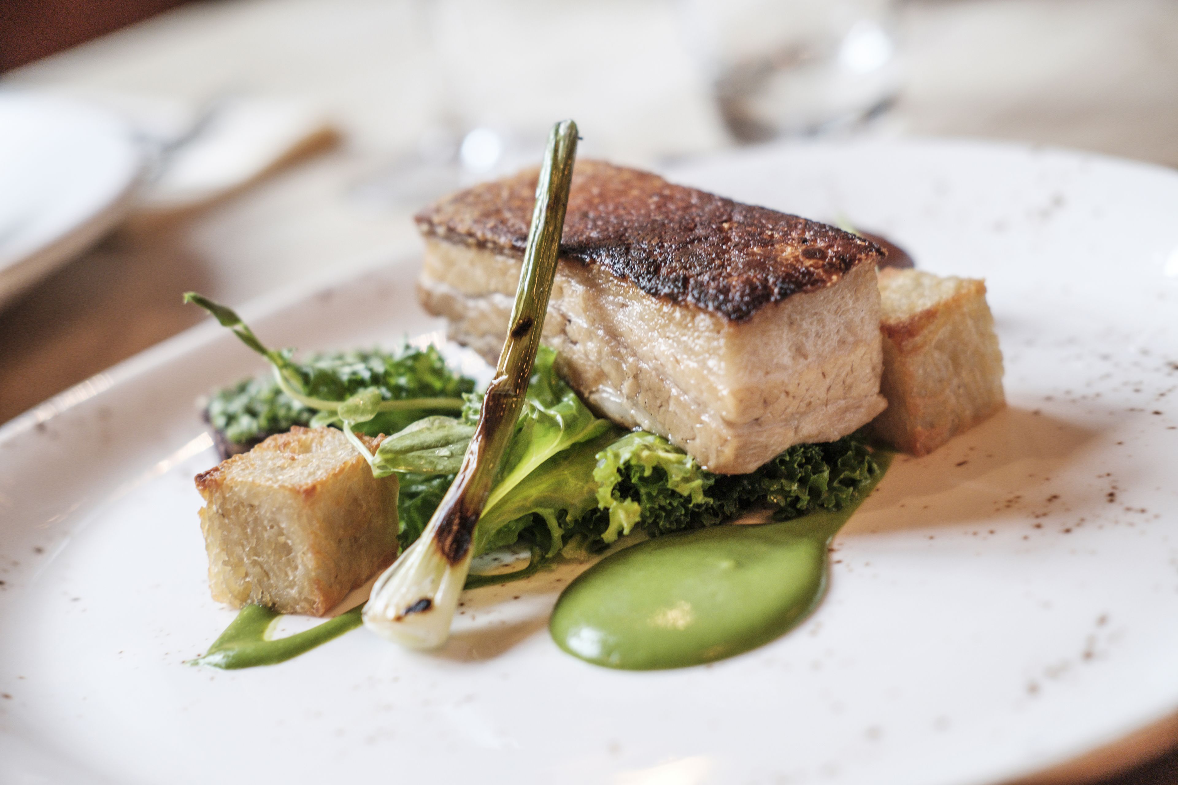 A plate with a piece of meat, greens, and a small bread-like item.