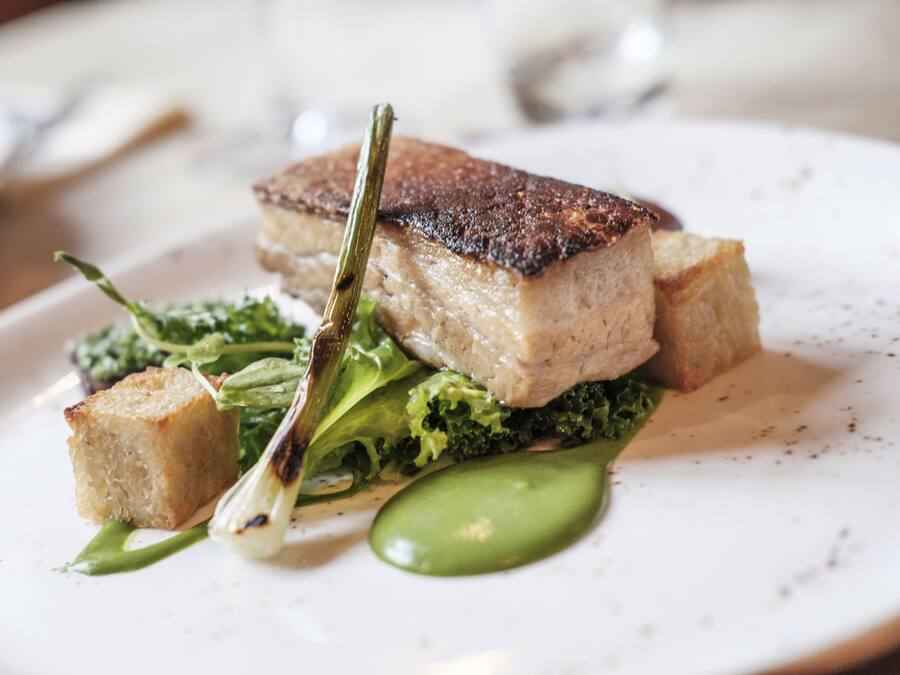 A plate with a piece of meat, greens, and a small bread-like item.