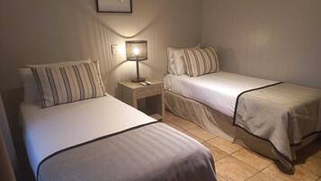 A hotel room with two single beds, a nightstand with a lamp, and a framed picture on the wall.