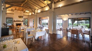 Un comedor amplio con varias mesas y sillas, una chimenea y ventanas grandes que ofrecen vistas al exterior.