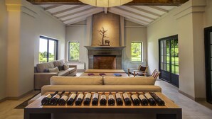Amplia sala de estar con chimenea, sofá, mesa de centro y una estantería para vinos con varias botellas.