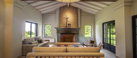 A spacious living room with a fireplace, a sofa, a coffee table, and a wine rack with multiple bottles.