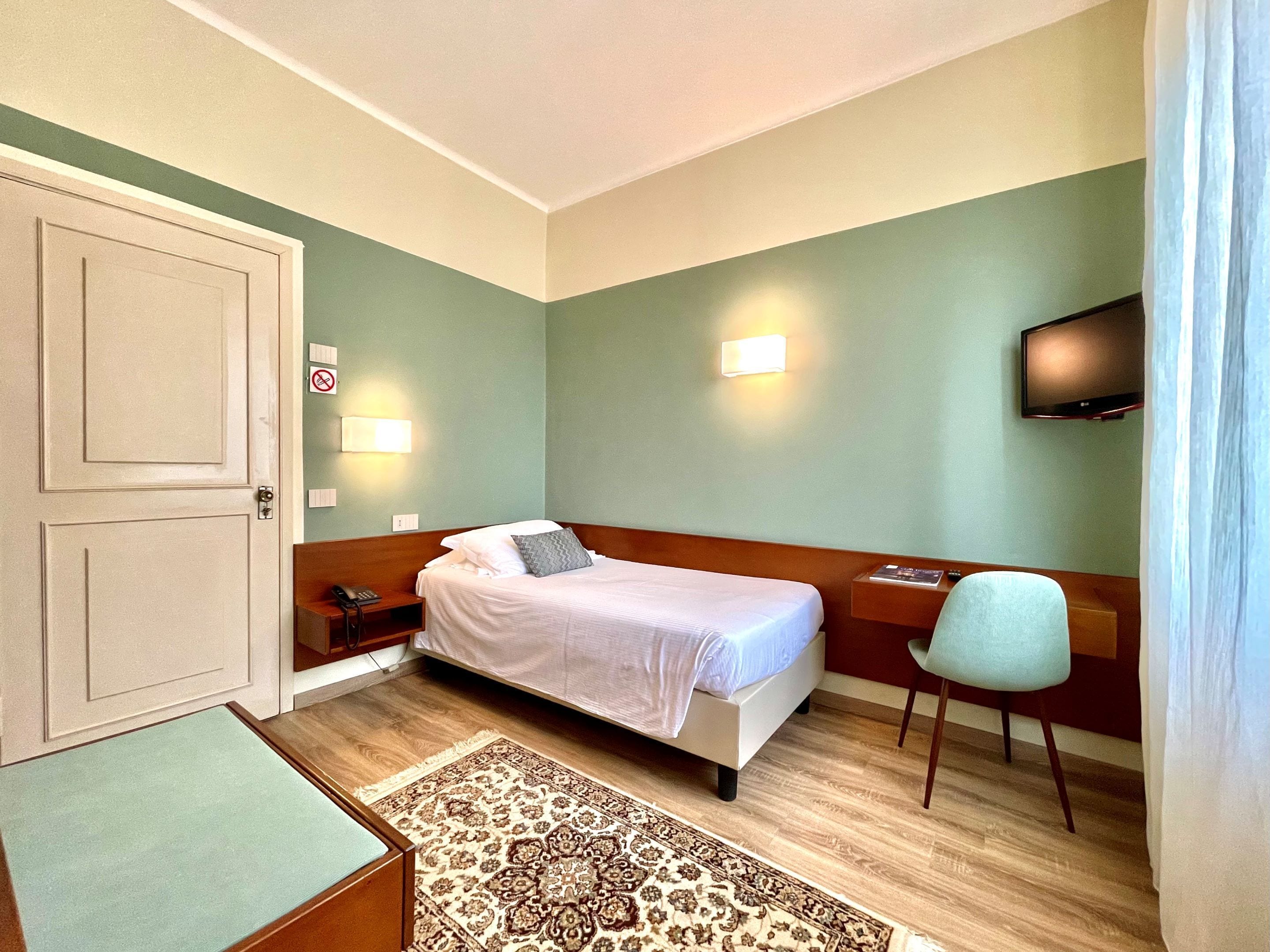 Ein Hotelzimmer mit Bett, Nachttisch, Stuhl, Fernseher und einer Tür.