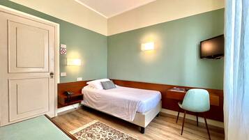 A hotel room with a bed, bedside table, chair, TV, and a door.